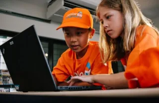 two children play at a computer wearing Junior Engineers branded hat and tshirts 