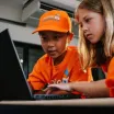 two children play at a computer wearing Junior Engineers branded hat and tshirts 