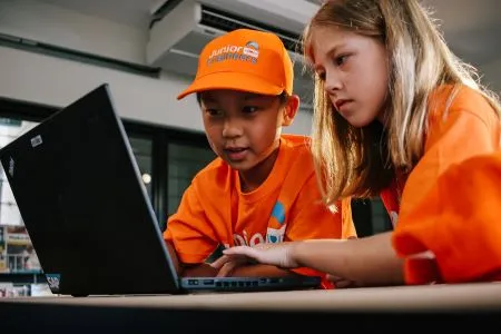 two children play at a computer wearing Junior Engineers branded hat and tshirts 